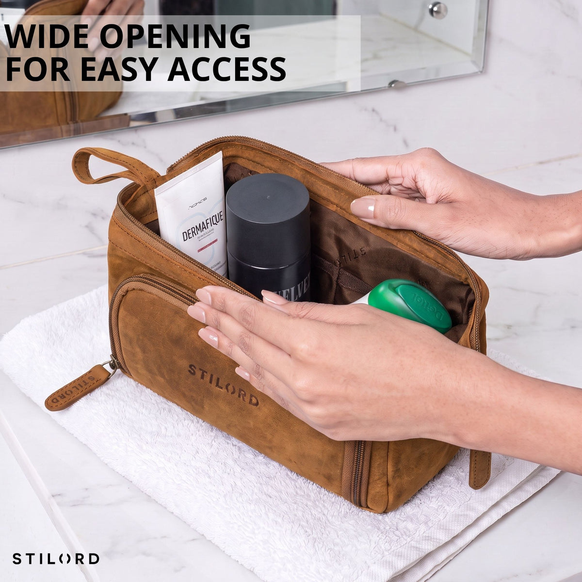 Leather toiletry bag in tan/dark brown, wide open with inner pockets visible, hands placing toiletries, STILORD logo
