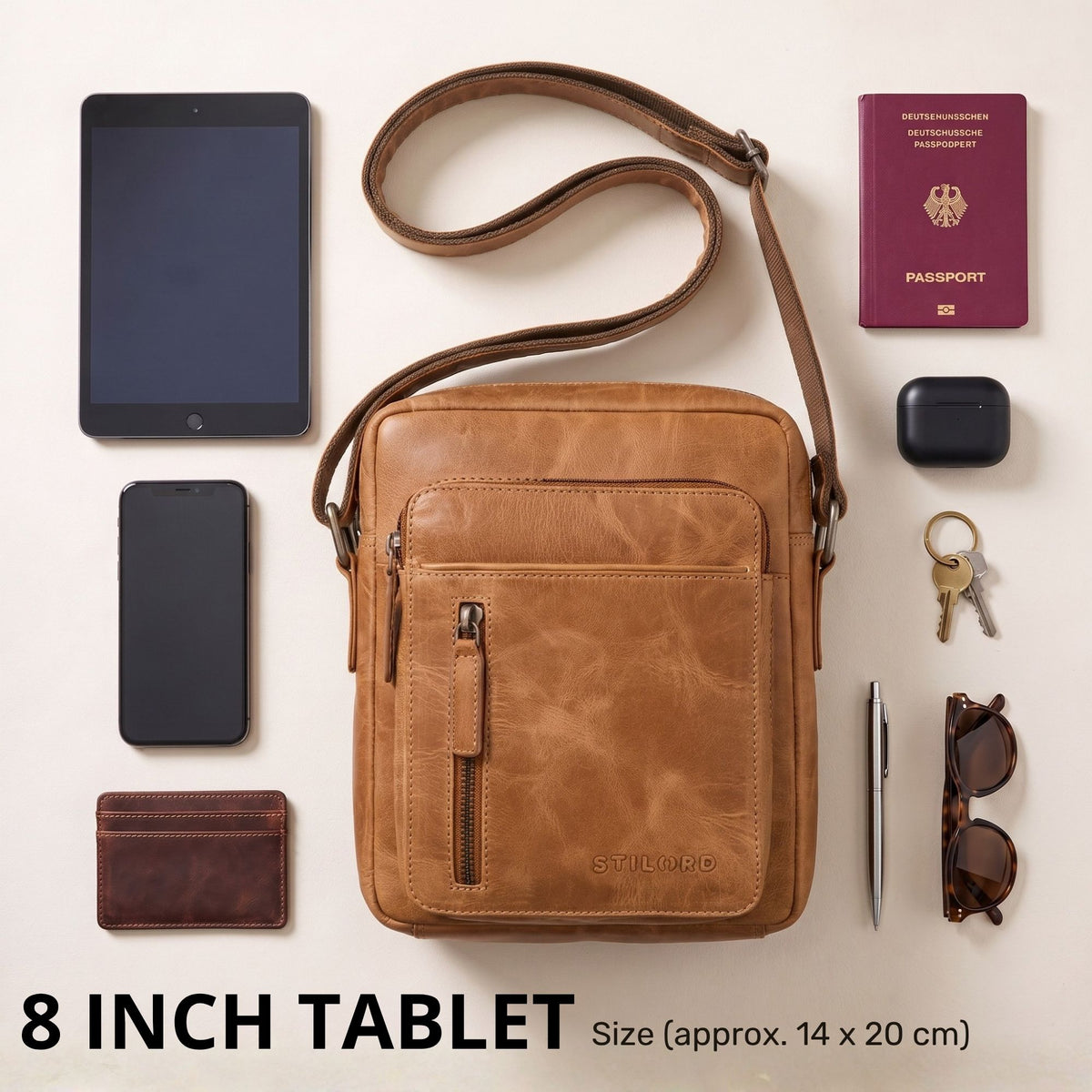Kleine Herren-Umhängetasche aus perugia-braunem Leder, Fronttasche und verstellbarer Schulterriemen, daneben 8-Zoll-Tablet und Reiseutensilien