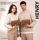 Two people hold Henry tan leather toiletry bag, front view with wrist strap and visible STILORD embossing
