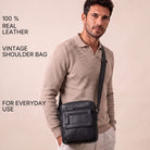 Slim black leather crossbody shoulder bag worn by man, front view, zip pockets visible, fits 8-inch tablet