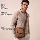 Small flat brown leather shoulder bag worn crossbody by man, slim vertical design fits 8-inch tablet