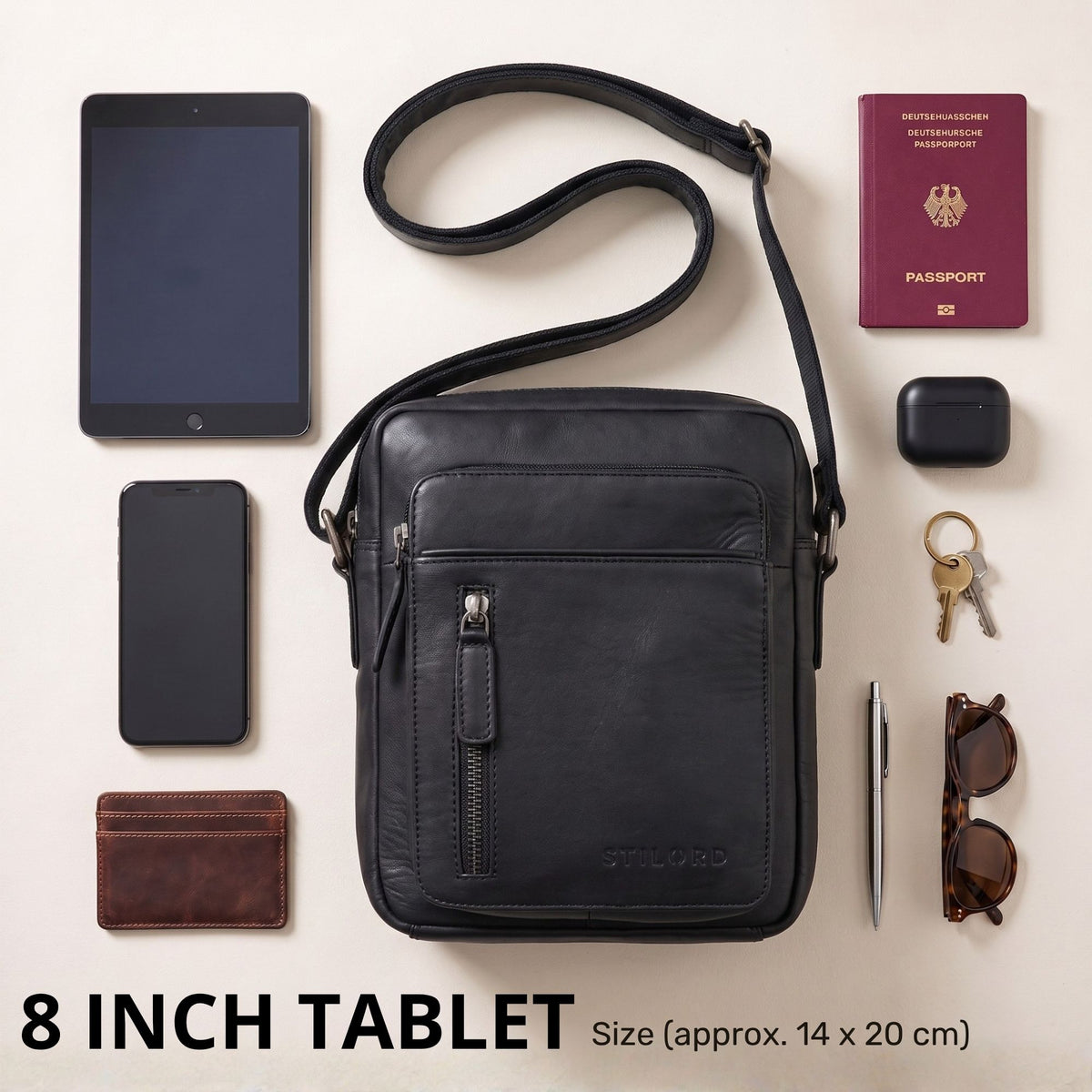 kleine schwarze Leder-Umhängetasche frontal mit Reißverschluss, daneben 8-Zoll-Tablet, Pass, Handy und Zubehör als Größenvergleich